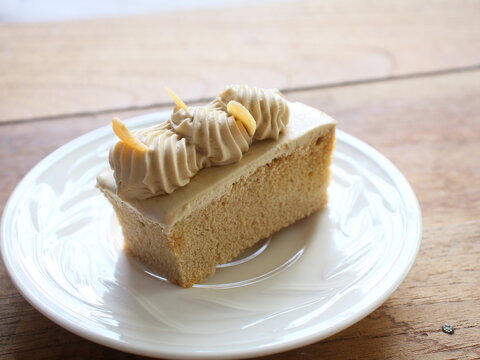Single slice of freshly baked coffee sponge cake with swirl coffee whipped cream and toasted almond toppings, served on a white dish. Ideal stock photo for cafe menus, coffee break concepts.