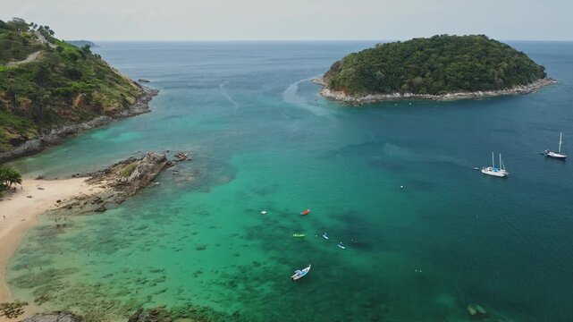 Tropical Thai island bay at Yanui Beach with clear turquoise water, sandy shore, lush green hills, and sailboats anchored nearby. Idyllic aerial view of a tranquil vacation destination in Thailand