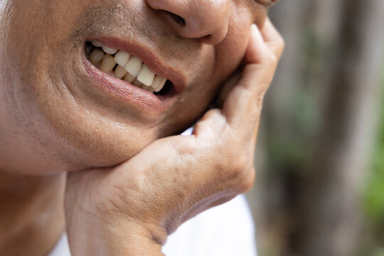 Old asian senior man with crooked teeth suffering from toothache, tooth decay, tooth sensitivity, teeth grinding problem, concept image for oral health care or dental care, mouth closeup shot