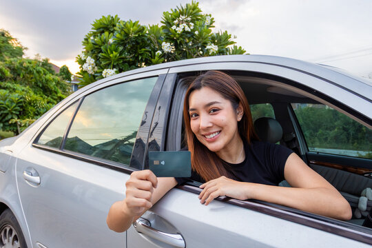 Happy female driver presenting payment card from car