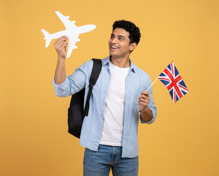 young indian man holding united kingdom flag and airplane cutout with backpack representing study abroad education travel immigration and uk visa opportunities