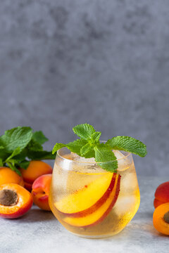 Cold summer beverage with sliced fresh nectarines, mint leaves, and ice in a condensed glass, garnished with fresh mint and fruit on a textured tabletop.