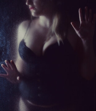 Mystisches Boudoir-Portr&auml;t einer Frau hinter beschlagener Glasscheibe. K&uuml;nstlerische Low-Key-Fotografie mit Schatten, Sinnlichkeit, Emotion, Fine Art und geheimnisvoller Atmosph&auml;re.