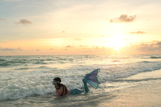 Girl in mermaid costume plays in ocean at sunset