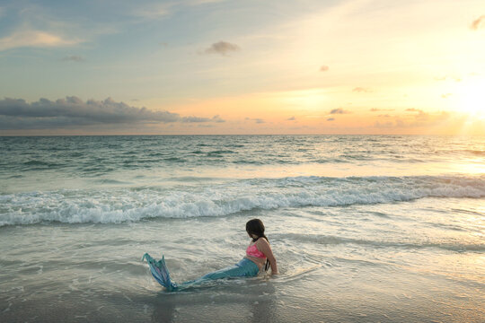 Little girl in mermaid costume watching sunset on beach