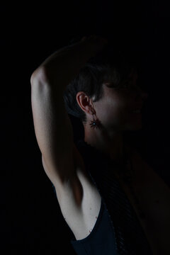 Low-Key-Portr&auml;t einer Frau mit erhobenem Arm und sichtbarer rasierter Achsel. Nat&uuml;rlichkeit, K&ouml;rperpflege, Beauty, Selbstbewusstsein, Minimalismus und Fine-Art-Fotografie.