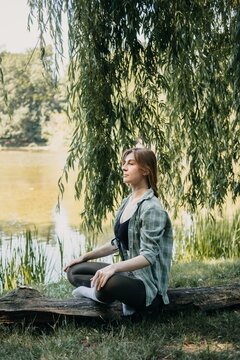 Woman meditating by lake under willow tree, forest bathing, breathwork exercise, grounding techniques, mental clarity