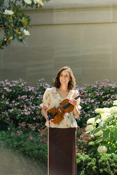 Smiling woman with violin stands in sunny garden
