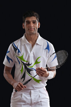 Portrait of confident young man with badminton racket over black background