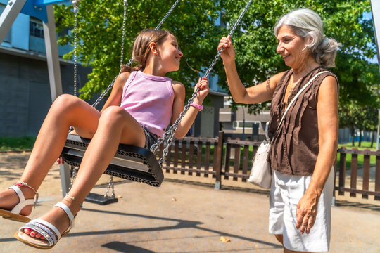 Grandmother pushing granddaughter on swing in playground