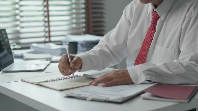 Businessman writing notes and analyzing financial documents at office desk