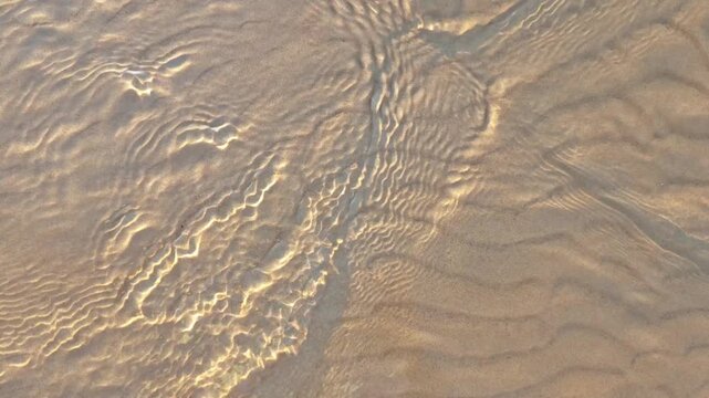 Waves moving on sand create patterns at the beach during sunset