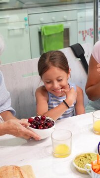 Happy family with a senior grandmother, mother, and little granddaughter enjoying a nutritious breakfast with fruits and juice, sharing a beautiful bonding moment together in the kitchen