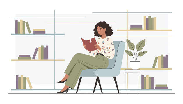 Young woman sits comfortably in a cozy armchair while reading an open book in front of bookshelves at home or in a library.