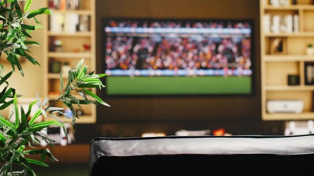 Empty living room with football game on television broadcast and couch facing large display in a home entertainment setup made of TV, cozy sofa and relaxed match night setting for home viewing.