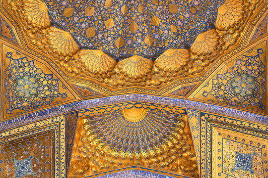 Ornate gilded ceiling of Ak Saray Mausoleum in Samarkand featuring muqarnas vaulting and blue floral tilework. Ideal for travel publications, cultural heritage features, and architectural design.