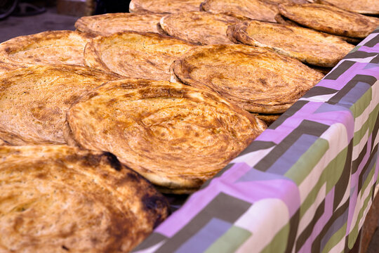 Rows of freshly baked traditional flatbread displayed at a bazaar in Bukhara, Uzbekistan. Warm golden loaves arranged on a colorful tablecloth, ideal for food culture and travel content.