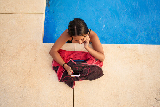 Young woman relaxing by swimming pool, browsing smartphone and connecting online during summer leisure time