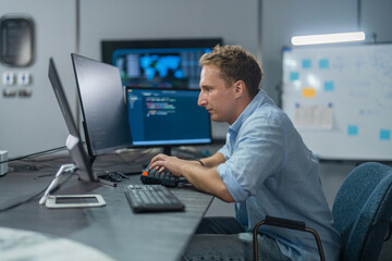 Fototapeta premium DevOps engineer, Caucasian male programmer working on computer monitors in modern IT office, software operations, system deployment, cloud infrastructure and advanced technology business innovation