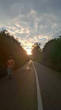 Woman walking alone on the road in the forest at sunset