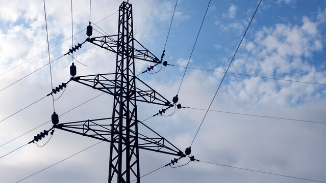 High voltage electricity pylon silhouetted against a cloudy blue sky. Supporting power lines and insulators for transmitting electrical energy across distances