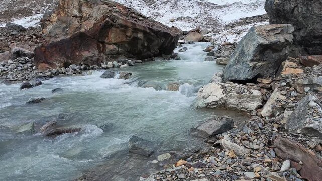 Glacial river flowing through rocky Svaneti mountains in Georgia, rushing cold turquoise water between stones and snowy peaks, wilderness landscape, travel destination