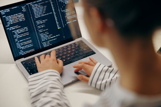 Close up of female software engineer writing code on laptop with screens setup in coworking