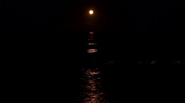 Strawberry moonrise full moon with orange hue and reflection over ocean surface