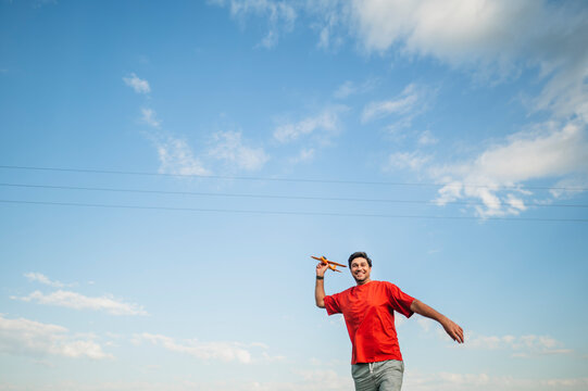 A smiling man launches a toy airplane against the summer sky