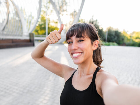 Happy young woman gesturing thumbs up at footpath