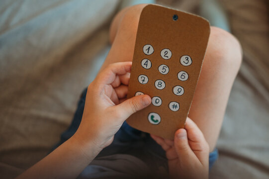 A boy holds a handmade cardboard phone at home