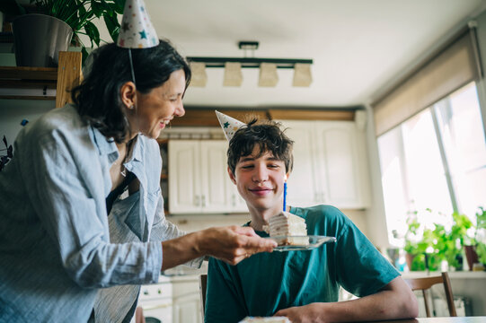 Mother gives birthday cake to her teenage son in the kitchen