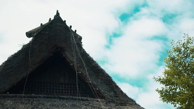 青空と雲に映える茅葺き屋根の重厚な頂部と伝統美 4Kシネマティック映像素材