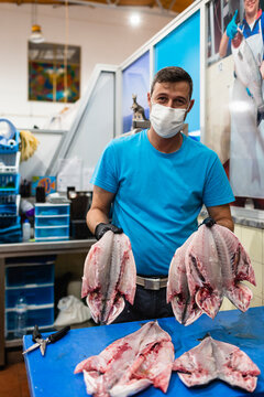 Fishmonger wearing mask holding fresh seabream in indoor market