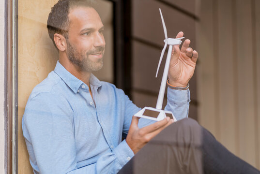 Businessman with wind turbine model behind windowpane