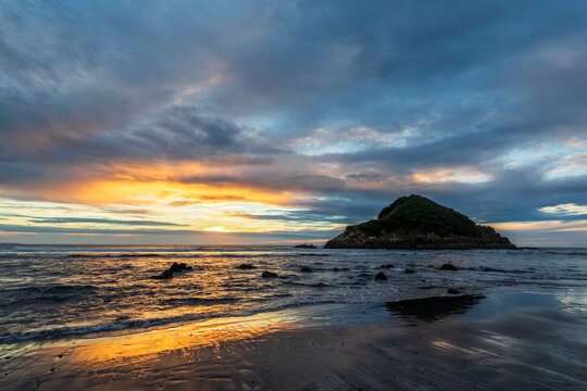 New Zealand, Tongaporutu, Cloudy sky over sandy coastal beach at sunset with Motuotamatea island in background
