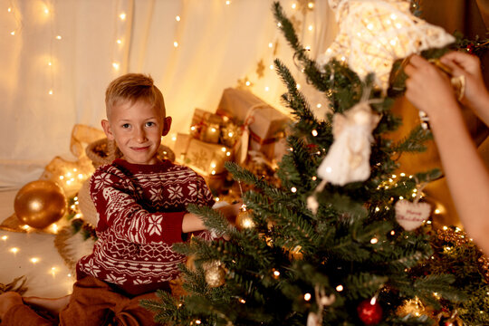 Smiling child in festive sweater decorating Christmas tree indoors