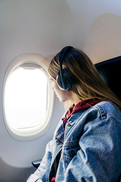 Woman wearing headphones looking out of window sitting in airplane