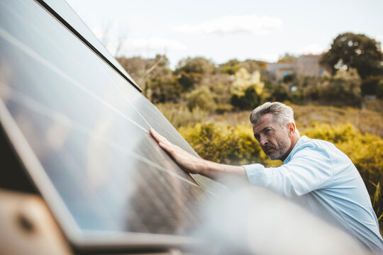 Mature man touching solar panel in garden