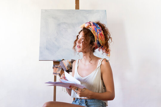 Young female painter in art studio next to empty canvas
