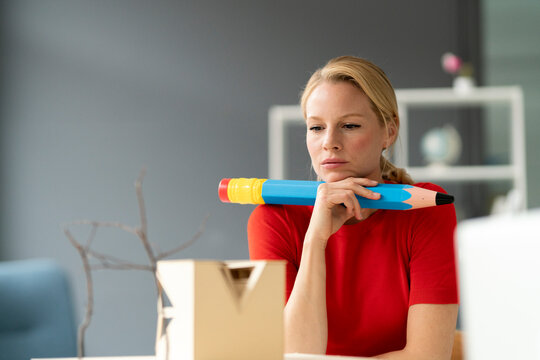 Young woman in office with oversized pen and architectural model on desk