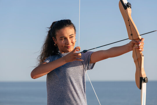 Determined young woman practicing archery on sunny day