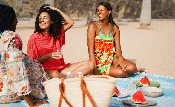 Happy multiracial girls eating watermelon and drinking fresh homemade lemonade while doing picnic on the beach - Summer and vacation concept - Main focus on center girl face - UGC content