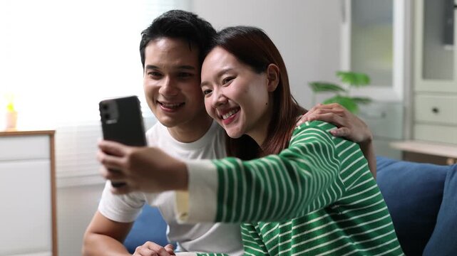 Asian couple are having fun taking selfies with their smartphones, having a relaxing time together.