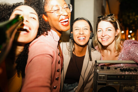 Group of multiracial girls having fun together drinking champagne and listening music outdoor - Party, nightlife and people lifestyle concept - Main focus on center latin girl face