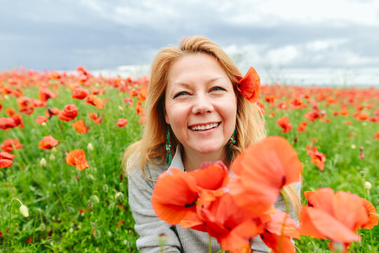 A mature woman smiles in a red poppy field enjoying nature