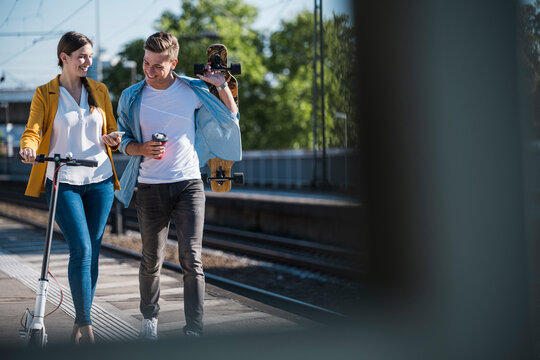 Young couple walks with scooter and longboard at the train station