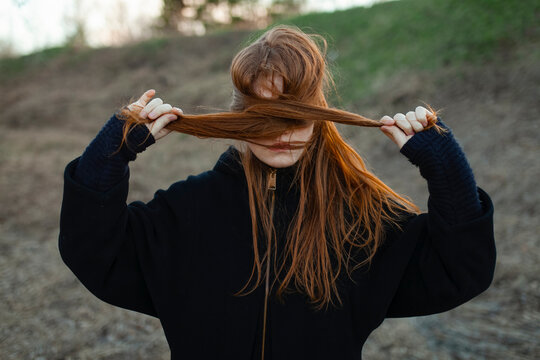 Girl holding red hair across face in sunny spring park