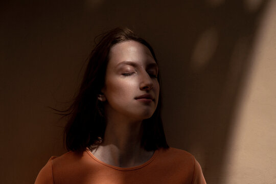 Young woman with eyes closed in front of wall