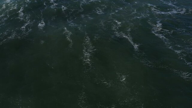 Aerial tilt down to waves flying back to sand